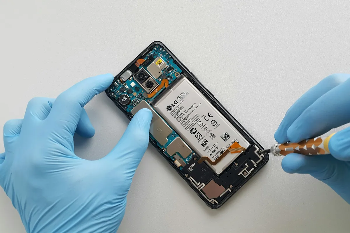 Remplacement de la batterie d'un smartphone par un technicien en gants bleus