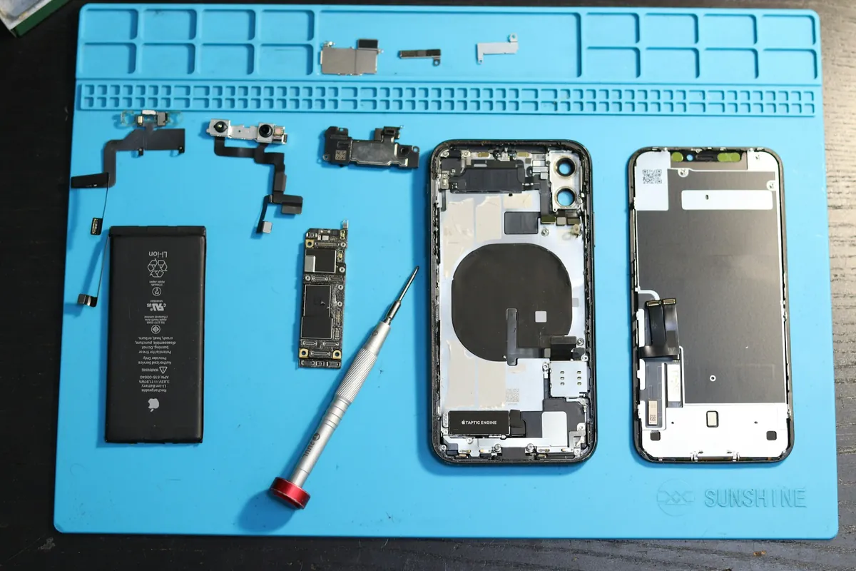 iPhone démonté sur un tapis d'atelier : batterie, écran et petites pièces