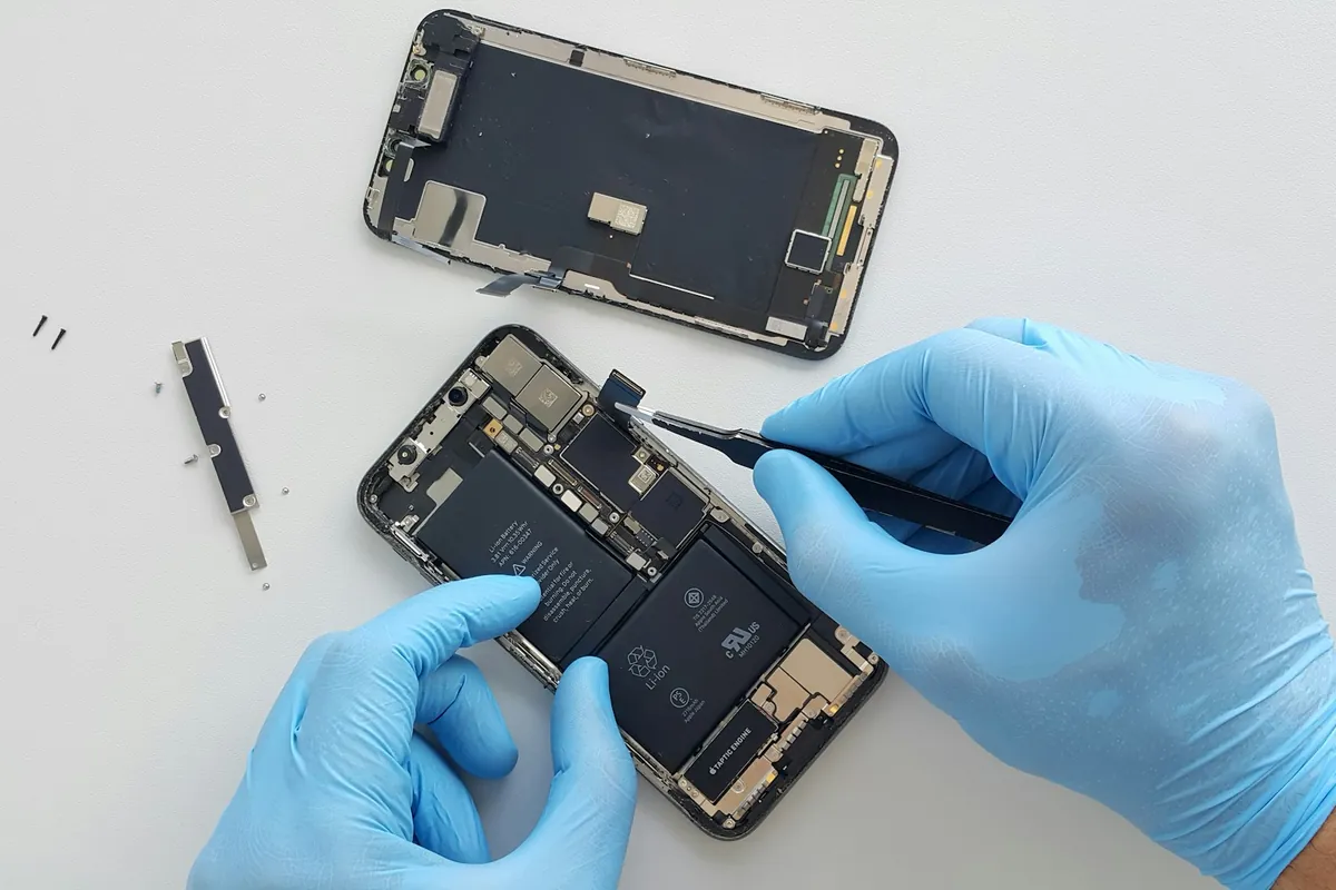 Technicien en gants bleus remplaçant l'écran d'un iPhone démonté