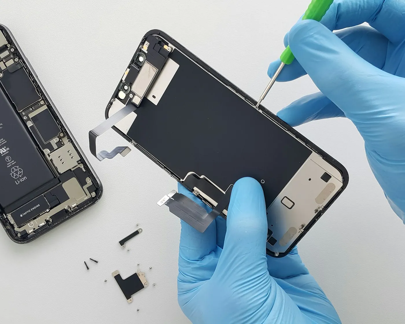 Réparation d'un écran d'iPhone : technicien en gants bleus soulevant l'écran avec un tournevis
